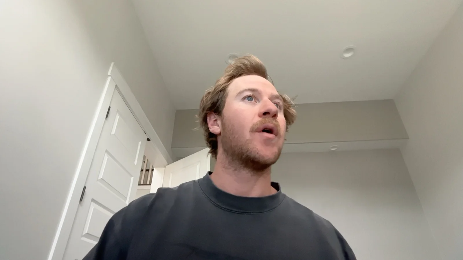 A man with tousled hair and a moustache leaning toward a laptop, seen from below by its camera, mid-word.